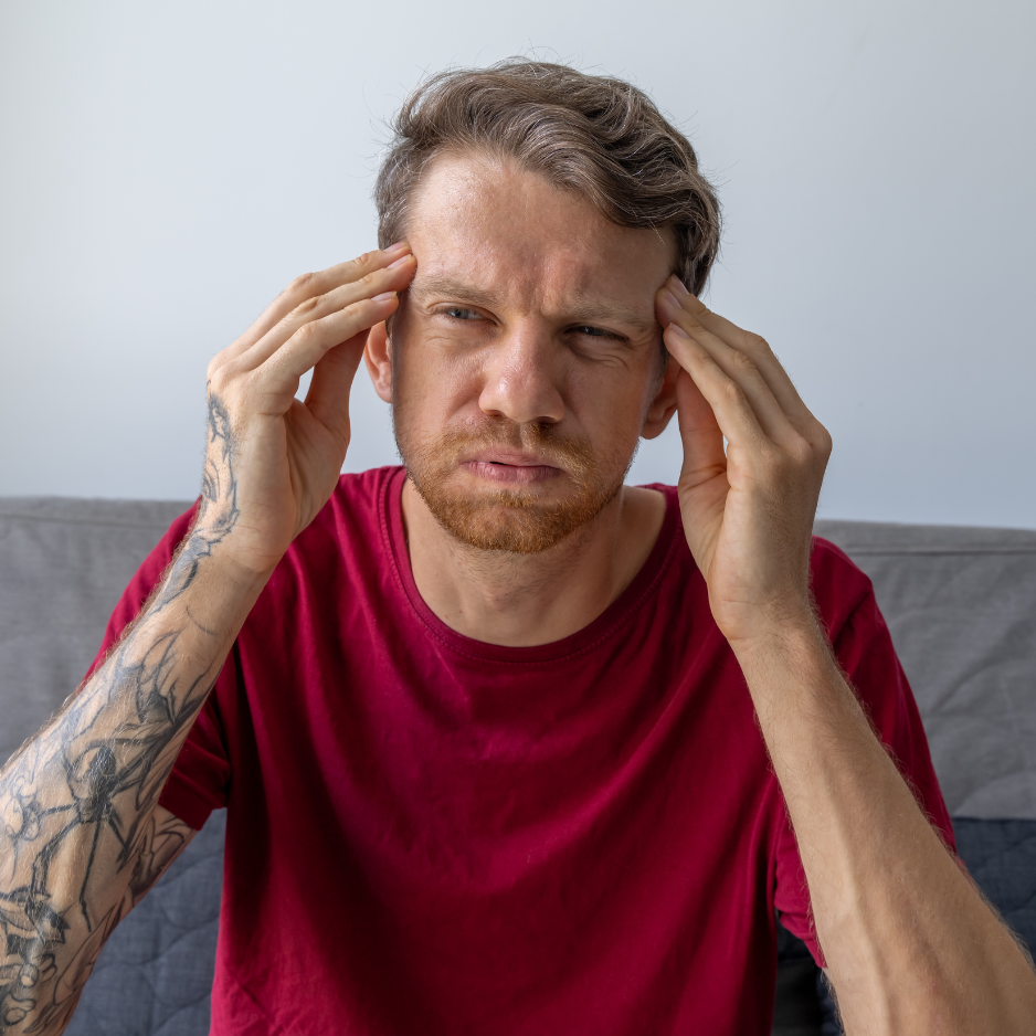 Man in red t-shirt with hands to his head struggling to think on a white and grey background