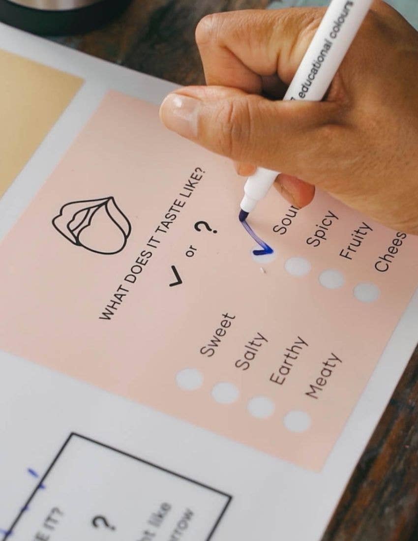 Hand using a marker to fill in a flavor profile chart on a pink sheet of paper.
