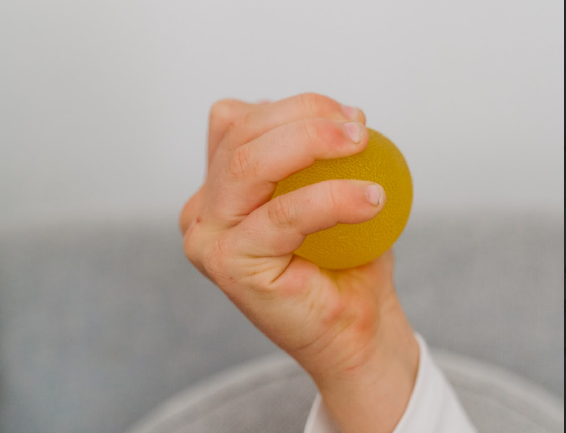 Hand holding a yellow stress ball against a plain background