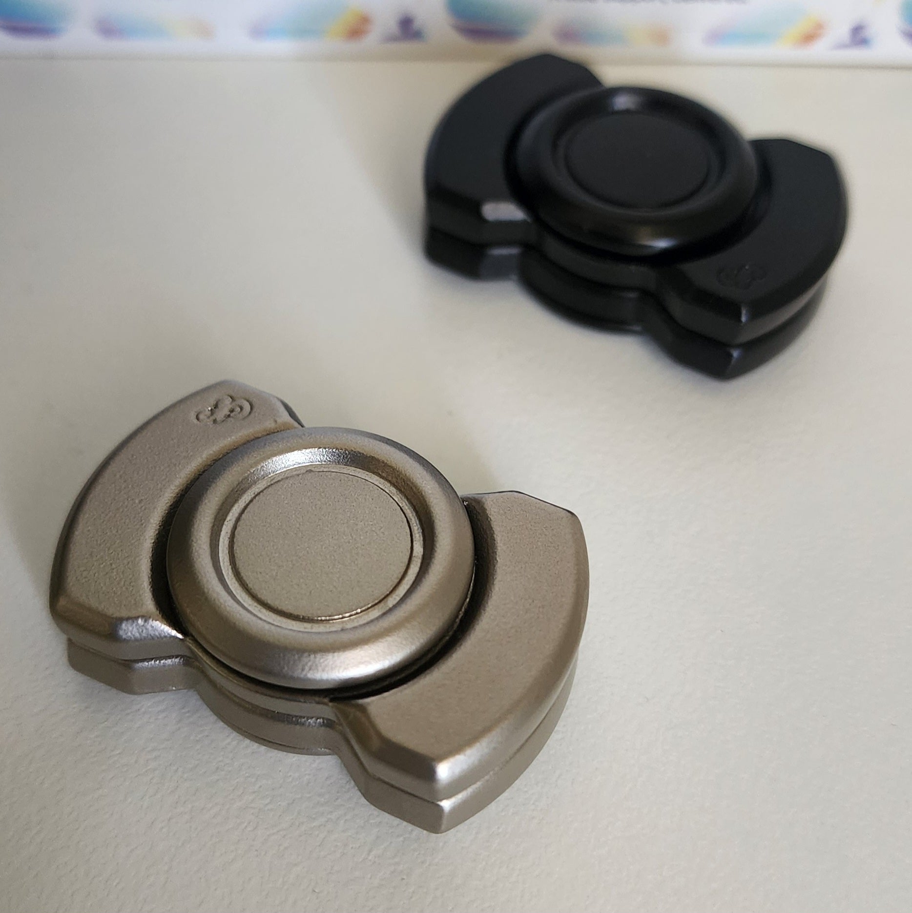 Two fidget spinners, one metallic and one black, on a light surface.