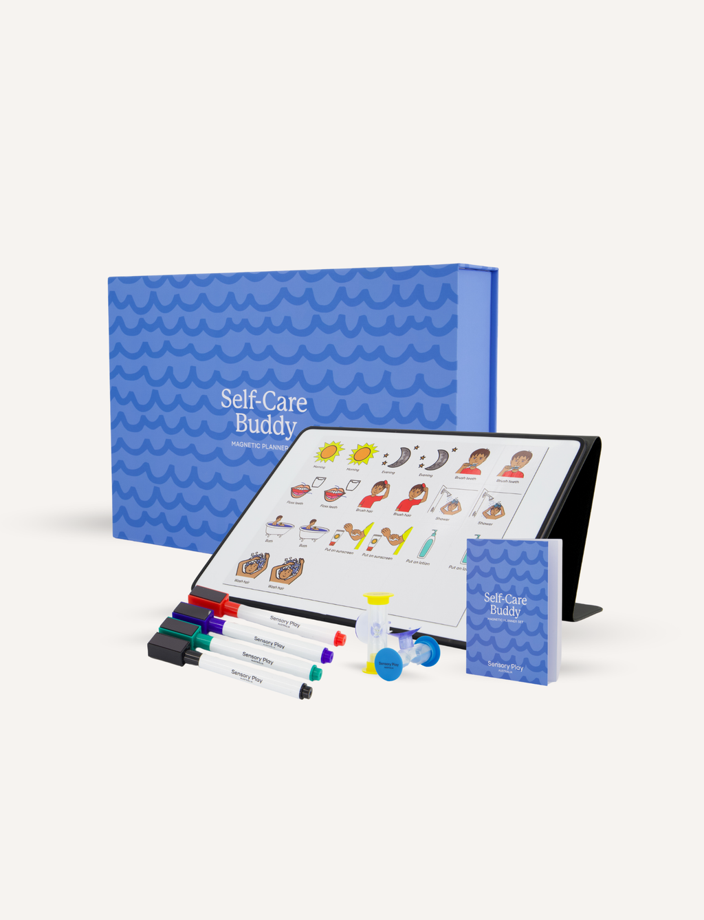Self-Care Buddy therapy kit displayed on a clean off-white background, featuring a tablet with illustrated self-care options, a blue patterned storage box, a small blue booklet, and several colored markers.